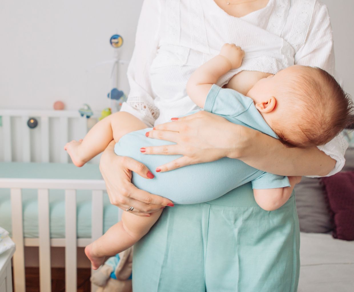Mother standing in a nursery breastfeeding her young baby, holding the baby close in both arms