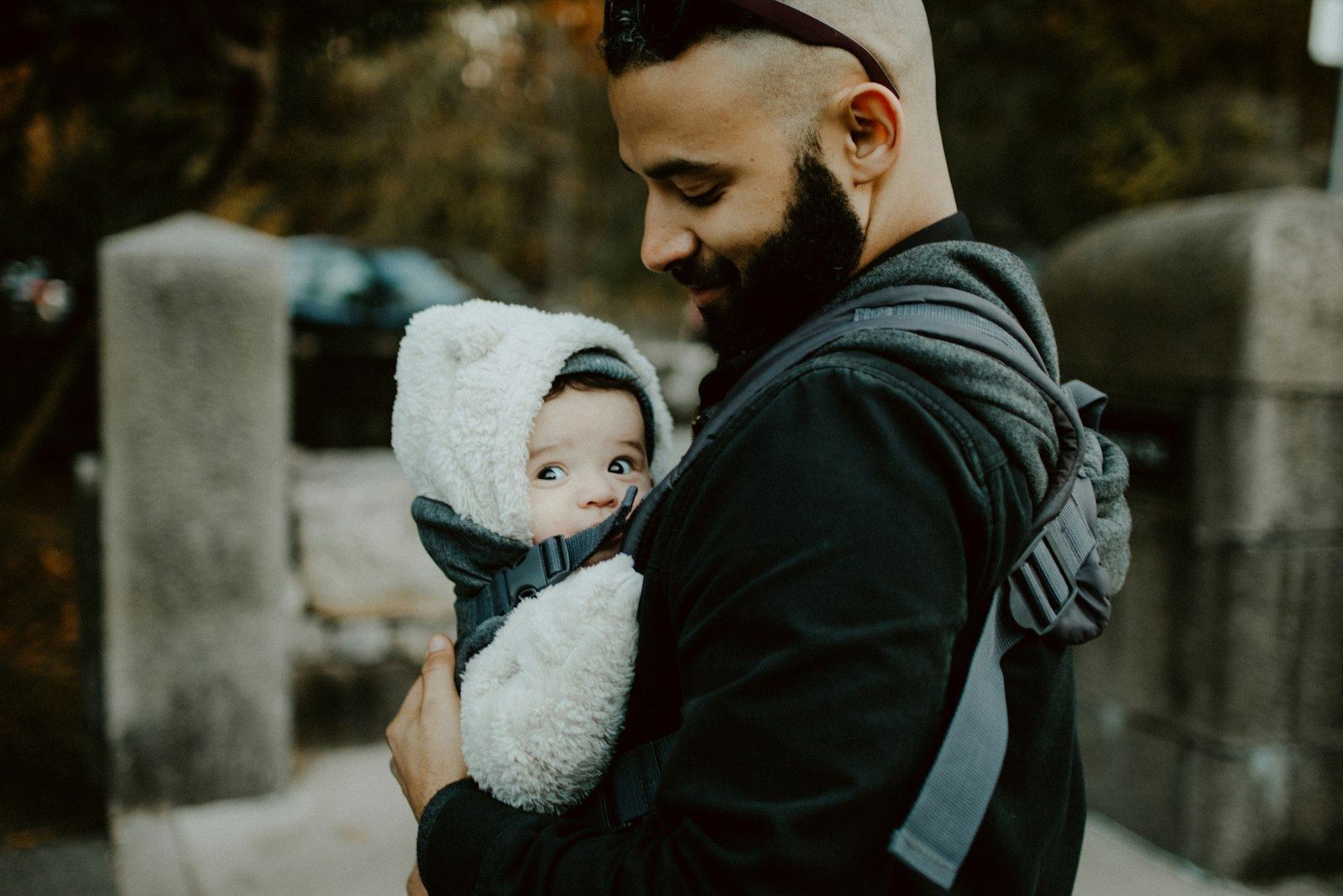 Father carrying a baby facing inward in a soft carrier, with the baby's face visible