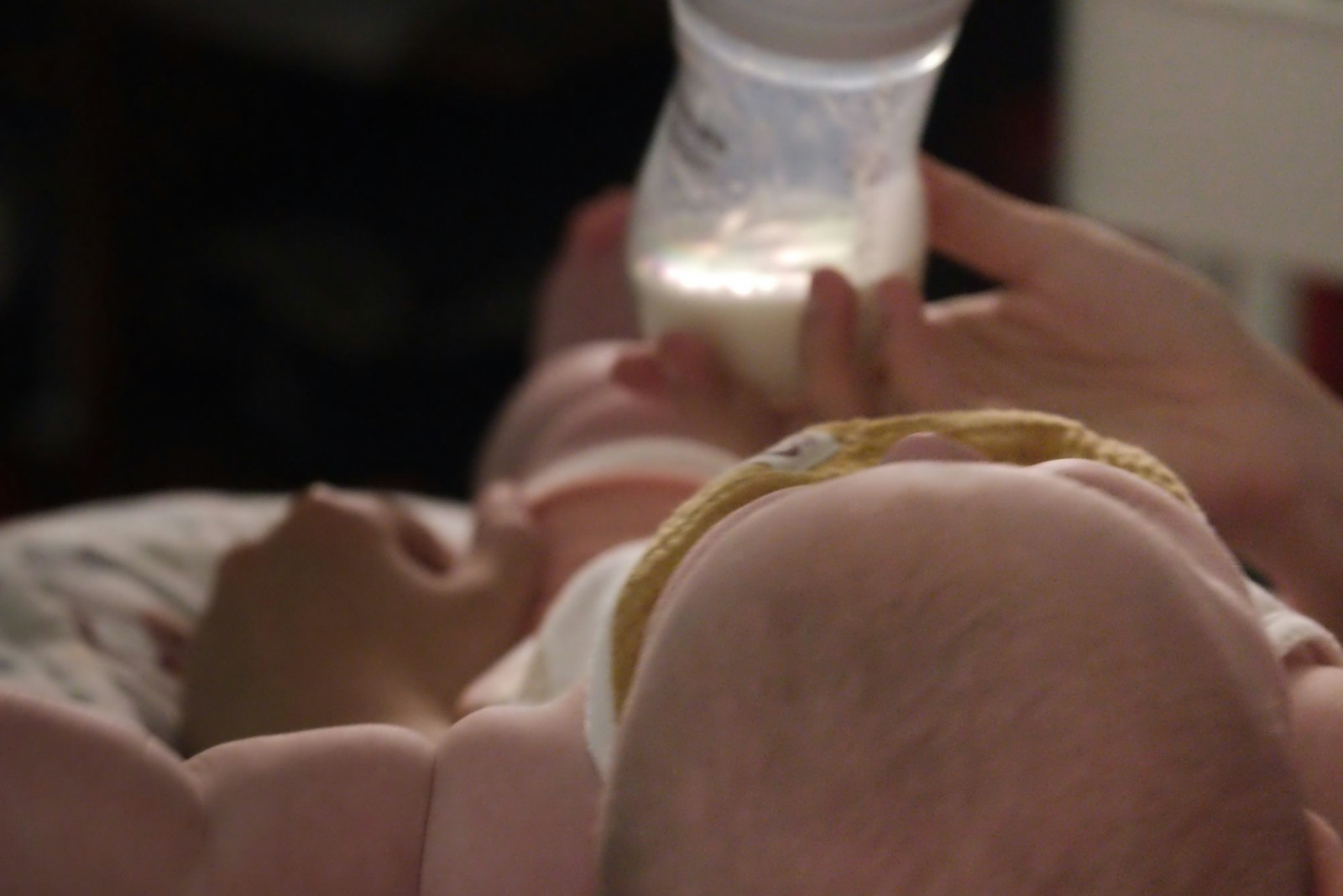 Baby drinking from a bottle held by a parent