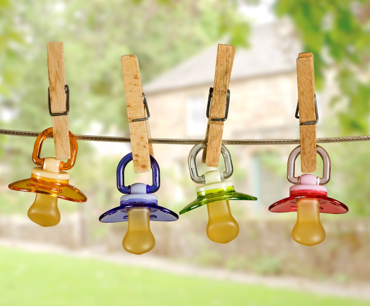 Four colorful baby pacifiers hanging from a clothesline with wooden pegs outdoors