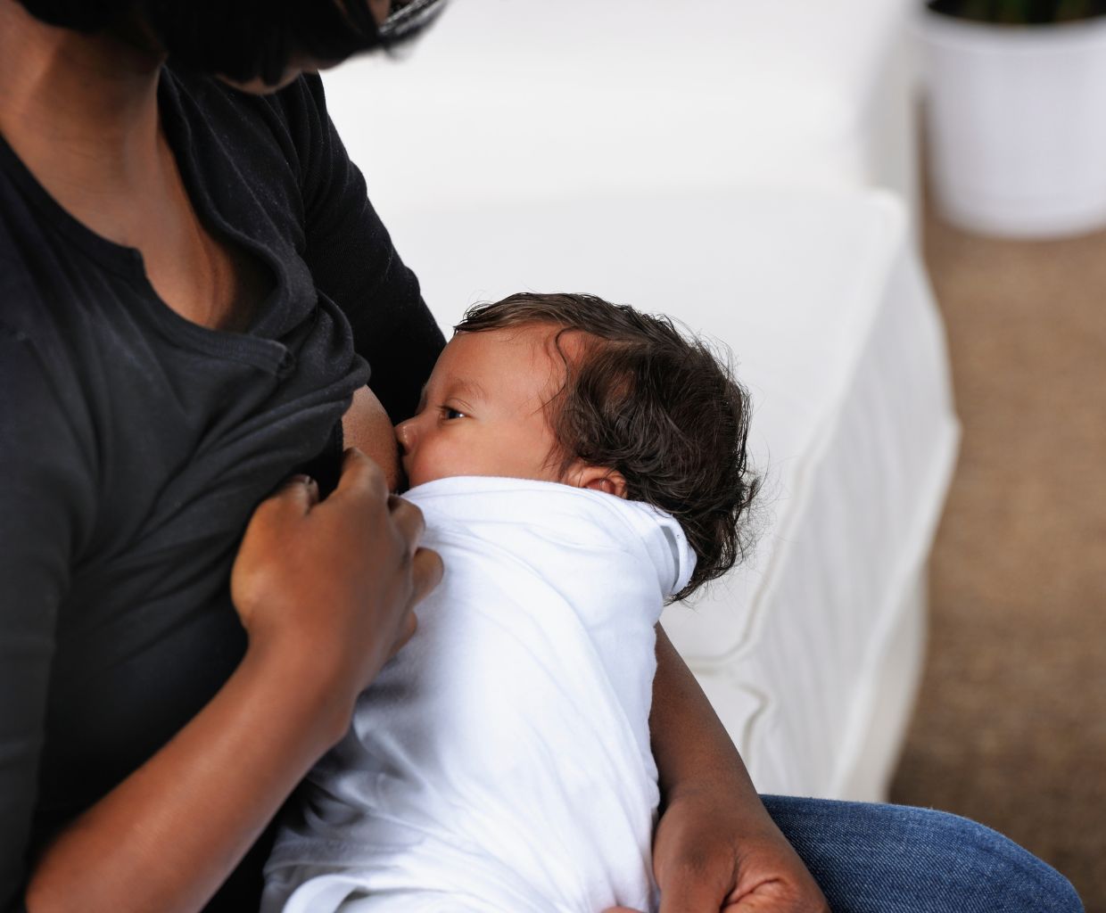 Mother breastfeeding her swaddled newborn while sitting on a sofa