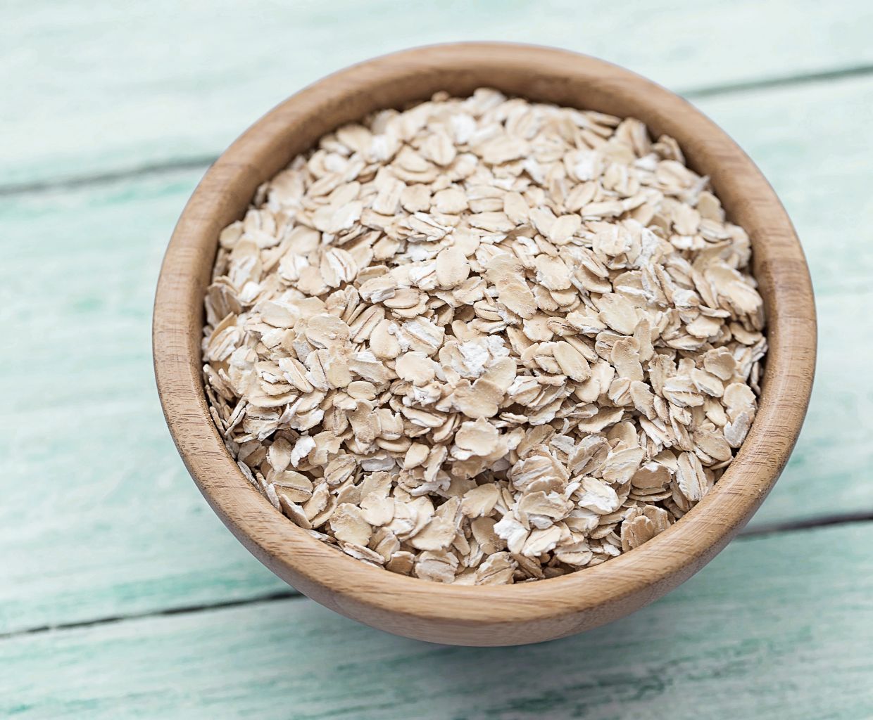 Wooden bowl filled with rolled oats on a pale blue wooden table