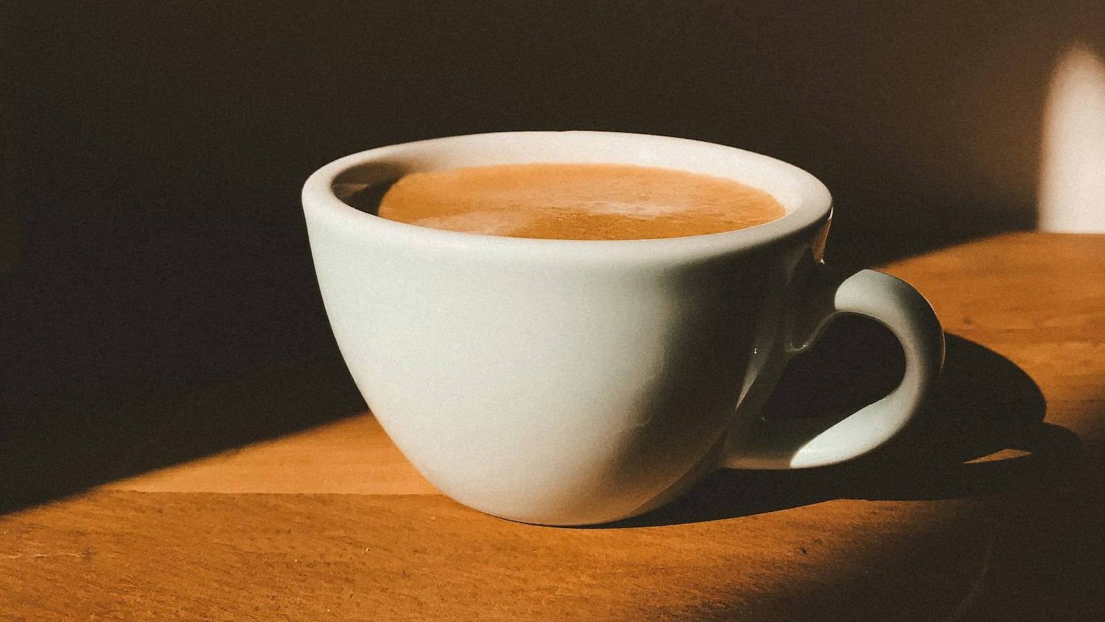 Cup of coffee with milk on a sunlit wooden table