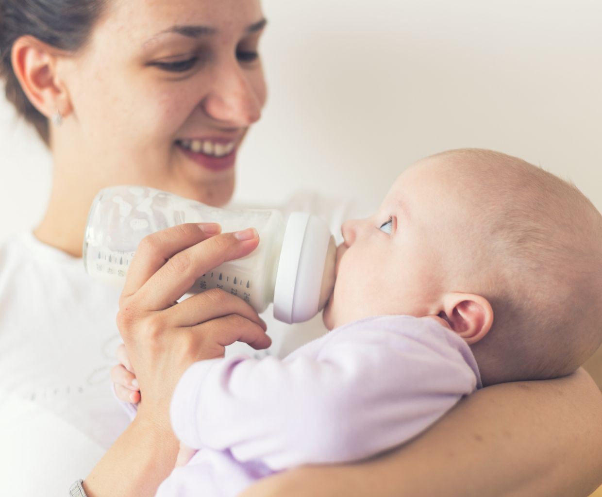Smiling mother feeding her baby a bottle of milk while holding the baby in her arm