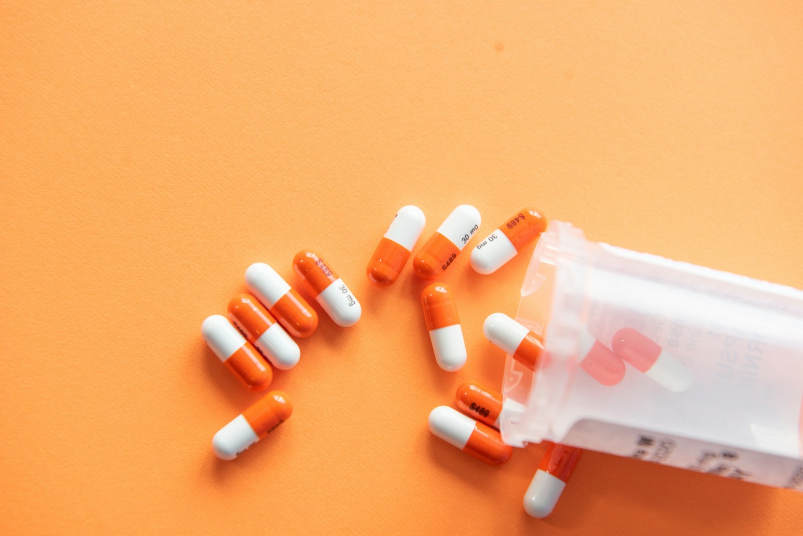 Orange and white capsules spilling from an open pill bottle