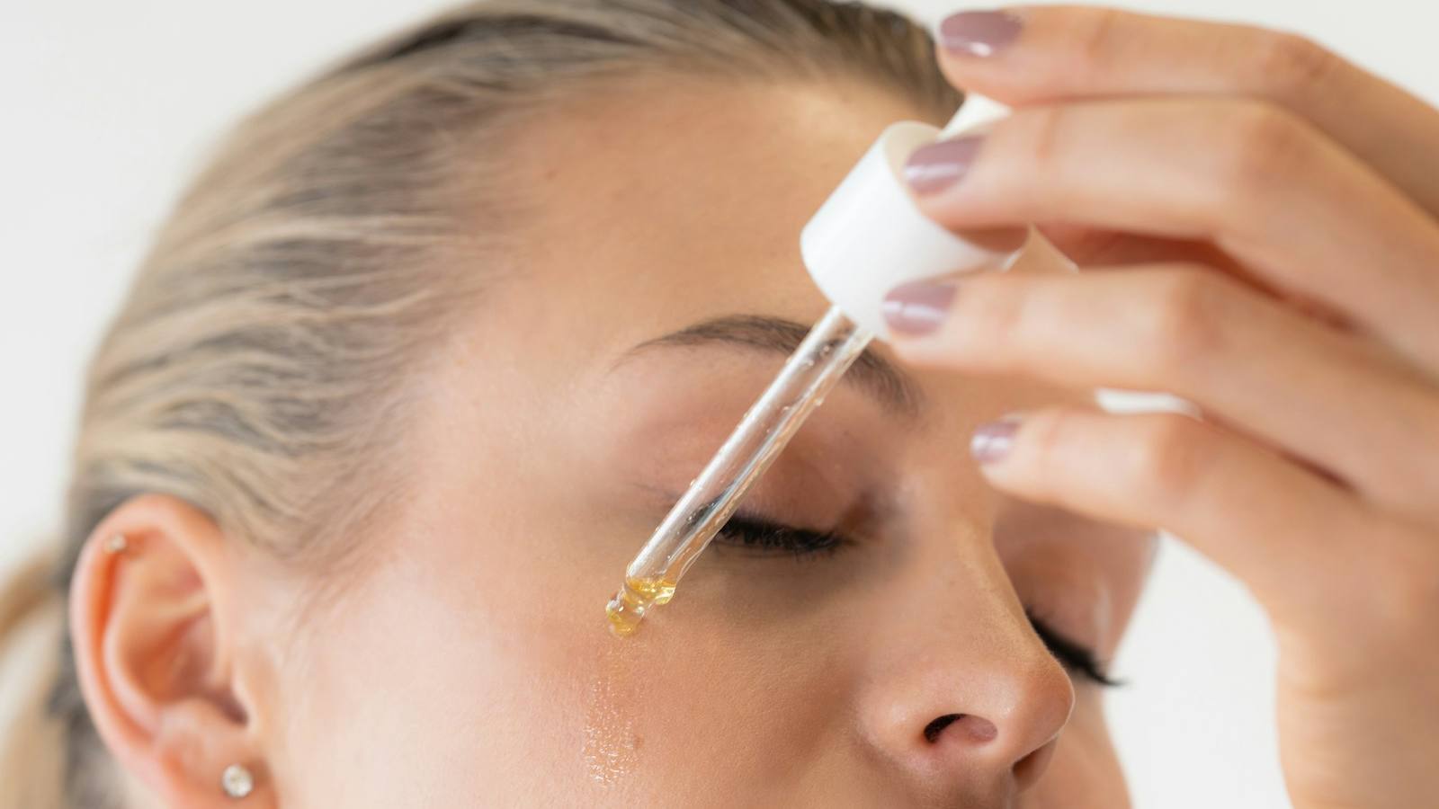 Woman applying a drop of serum to her forehead with a dropper