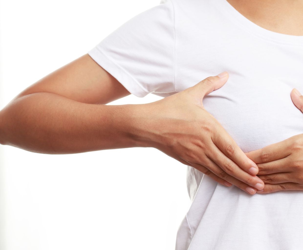 Woman in a white T-shirt pressing gently on a tender spot on her breast