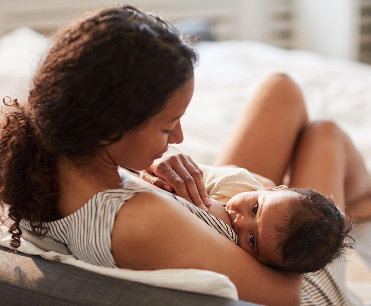 Mother resting on a couch while breastfeeding her baby at home