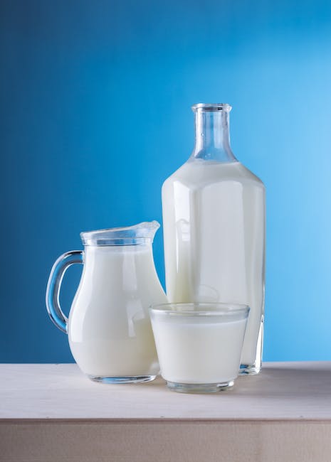 Glass jug, bottle and glass of cow's milk on a wooden table against a blue background