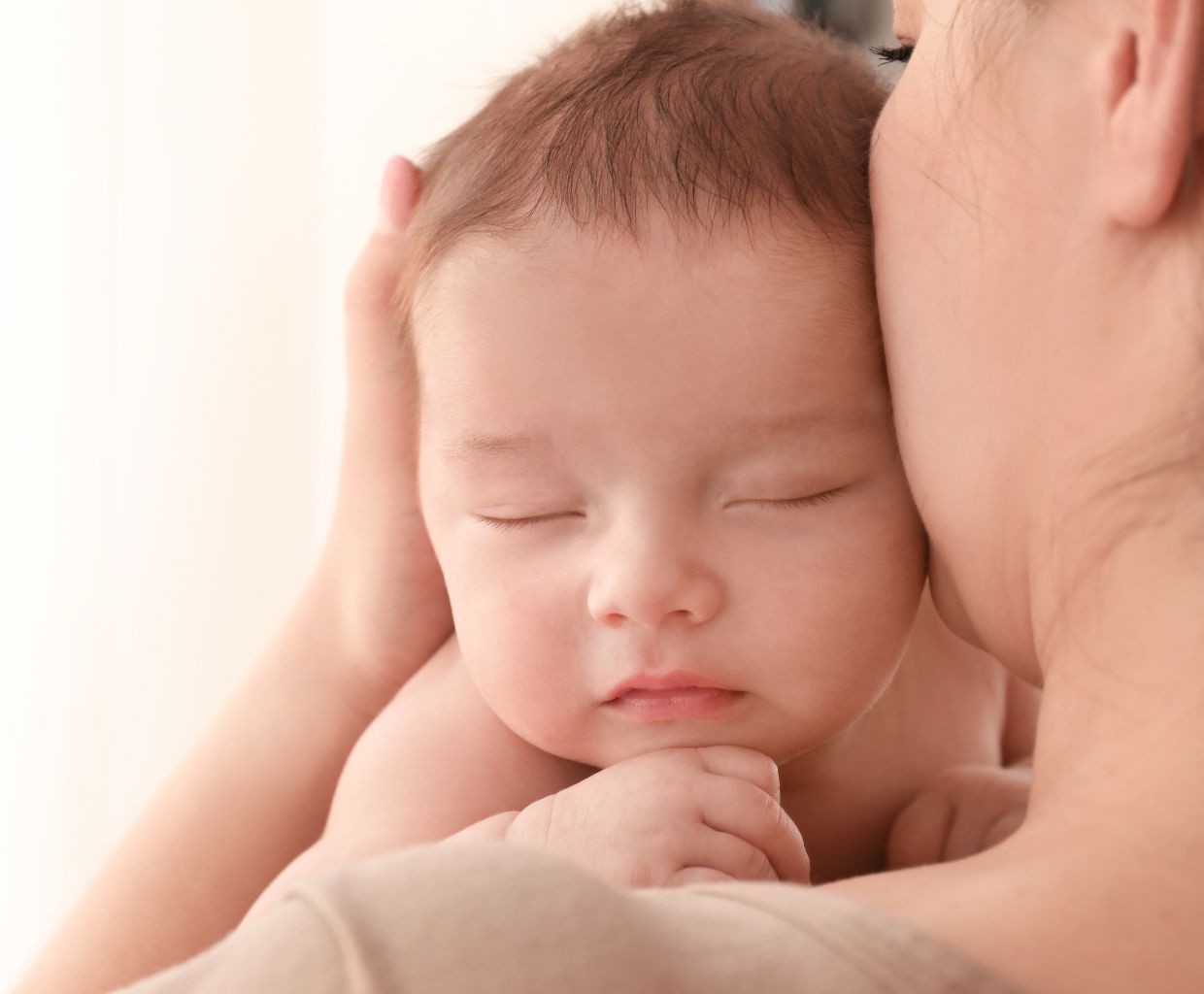 Mother resting her cheek against her sleeping baby's head with her eyes closed