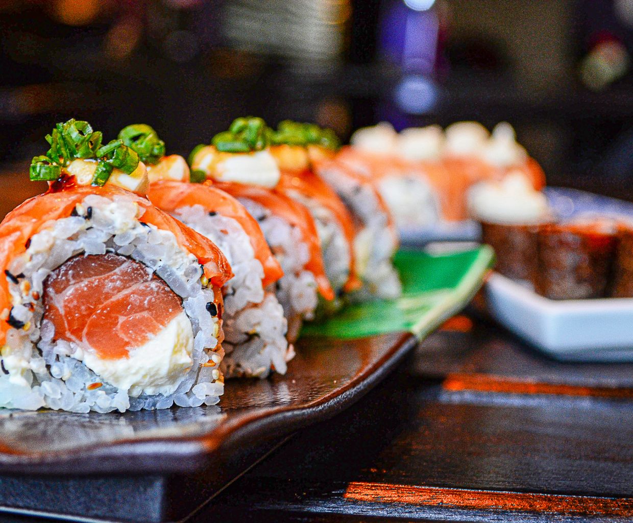 Salmon sushi rolls topped with green onion on a dark serving plate