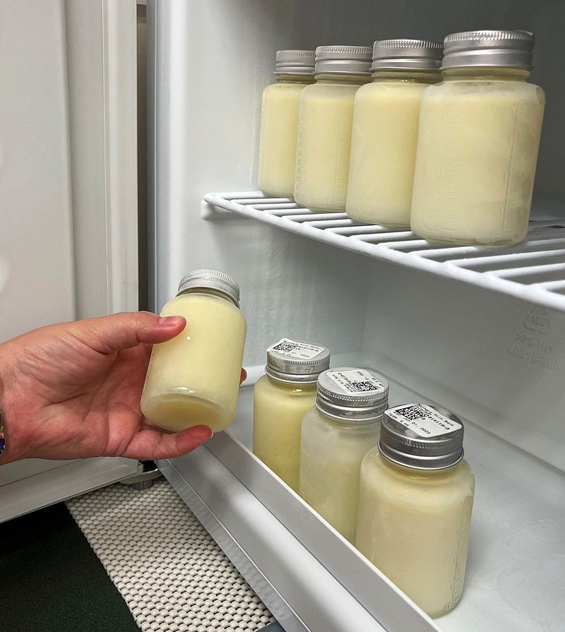Hand taking a jar of breast milk from a refrigerator shelf with more jars stored inside