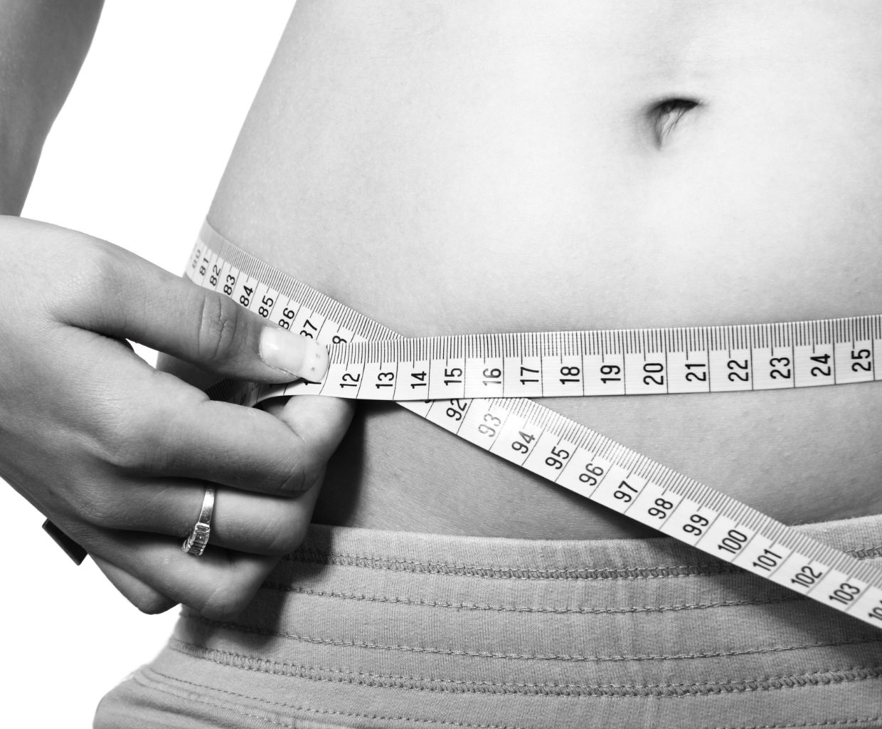 Black and white photo of a woman measuring her waist with a tape measure