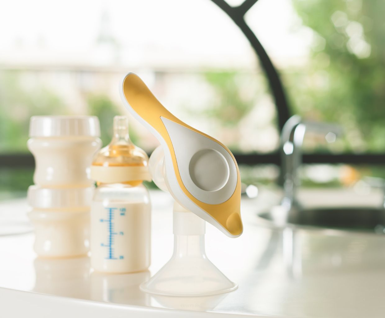 Manual breast pump and a bottle of milk on a kitchen counter next to the sink