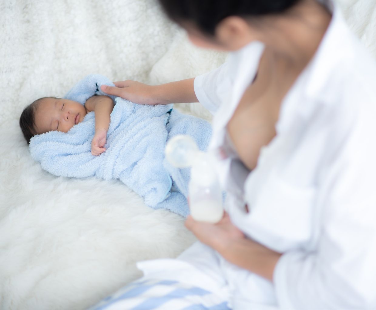 Mother holding a bottle of pumped breast milk beside her sleeping newborn