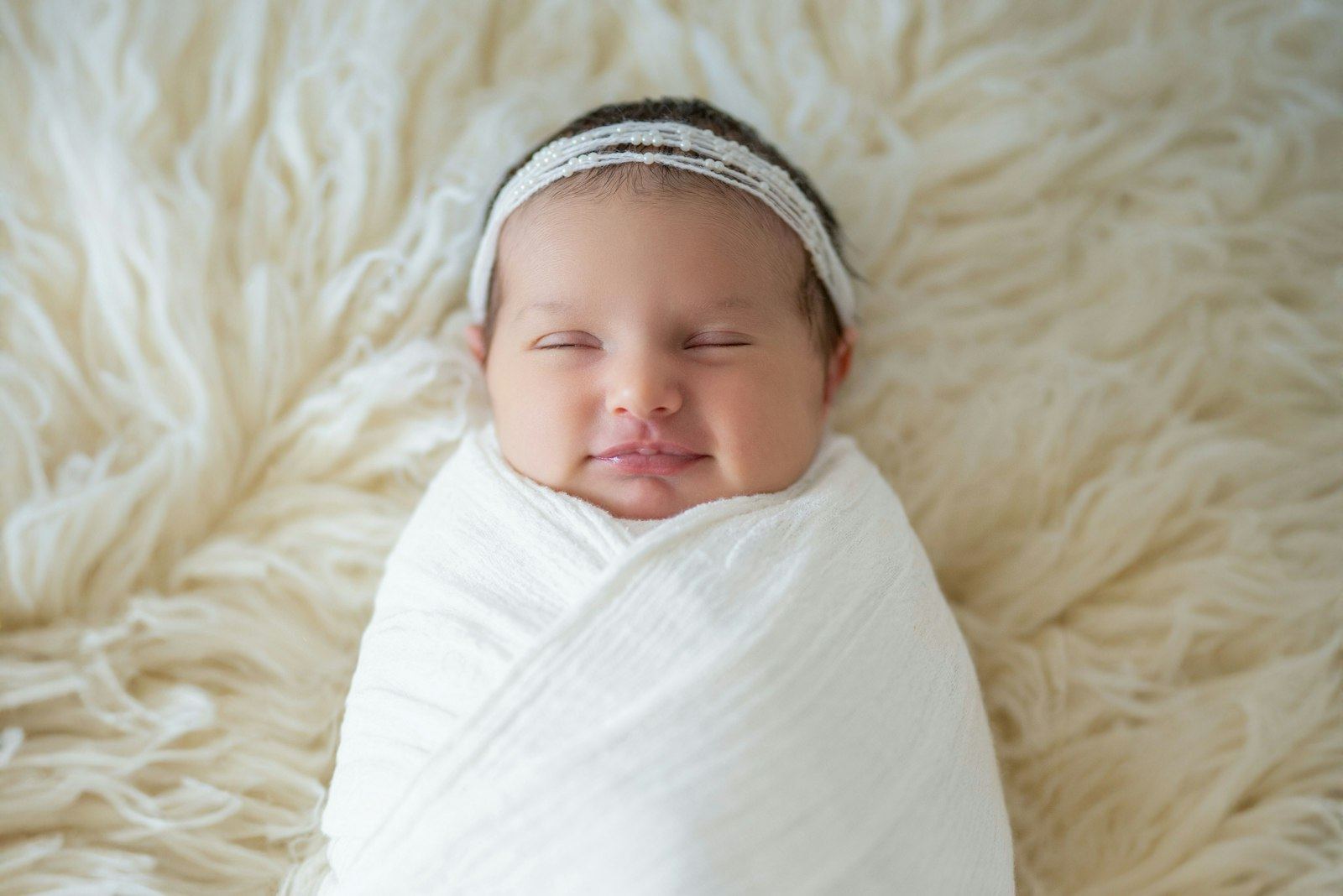 Smiling newborn swaddled in a white wrap, lying on her back