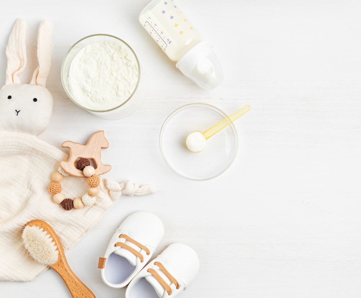 Bowl of white milk powder, a baby bottle and a scoop on a white table with baby toys