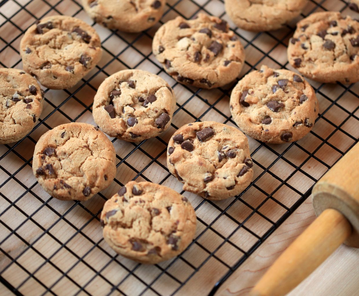 Freshly baked chocolate chip cookies cooling on a wire rack next to a rolling pin