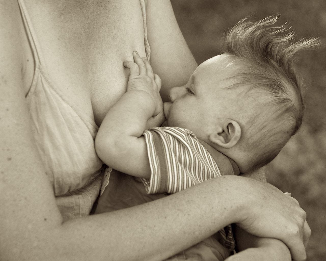 Black-and-white close-up of a baby breastfeeding with a hand resting on the mother's breast