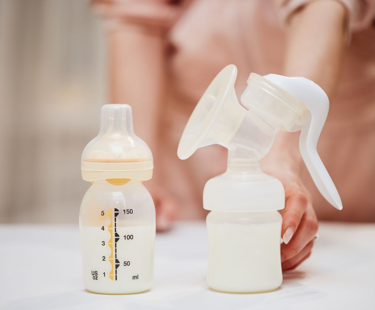 Manual lever breast pump with collected milk next to a baby bottle on a white table