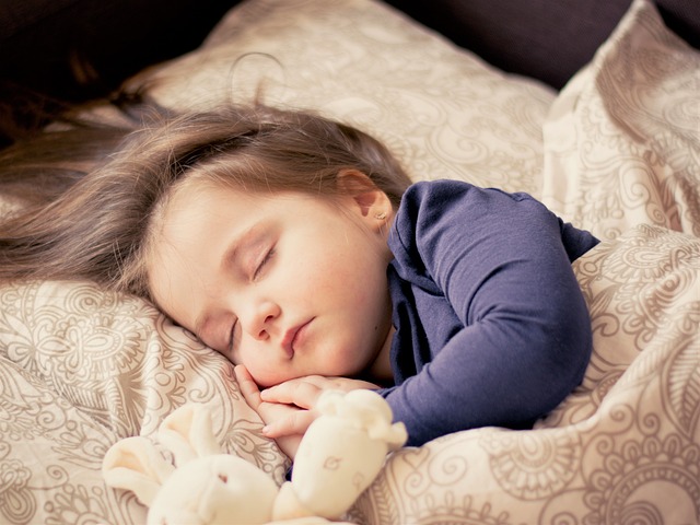 Toddler sleeping peacefully in a bed next to a soft toy