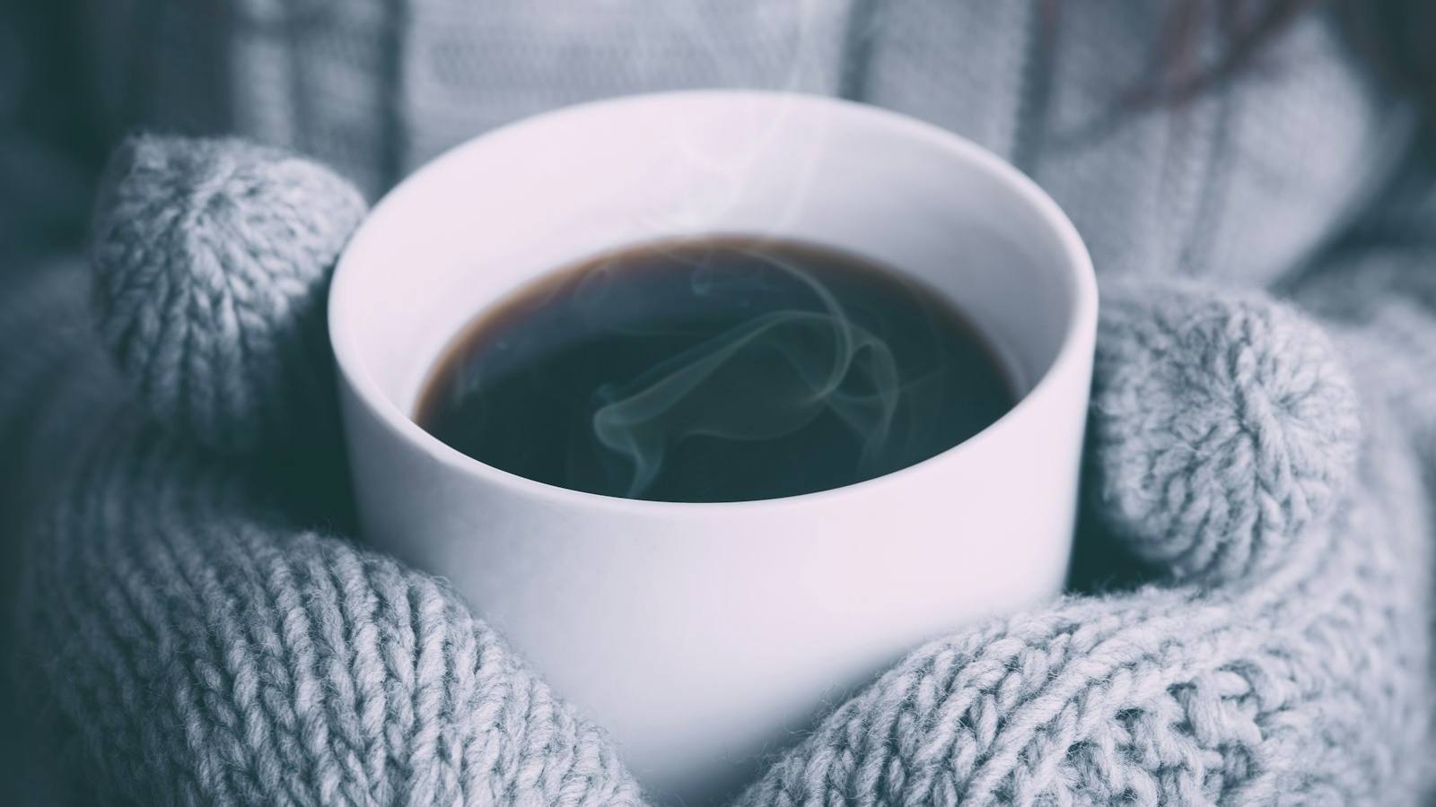 Hands in knitted mittens holding a hot cup to stay warm