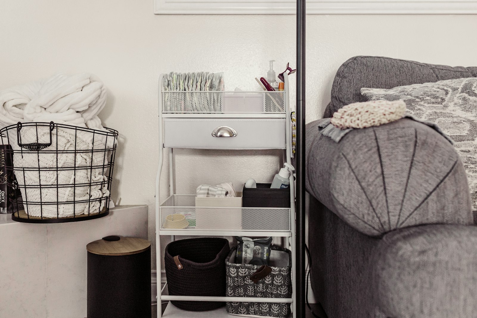 Storage cart with baskets of baby supplies next to a sofa