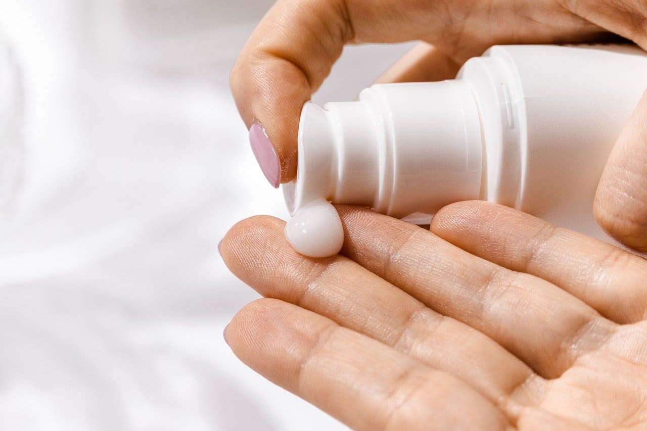 White lotion being pumped from a bottle onto a woman's fingertips