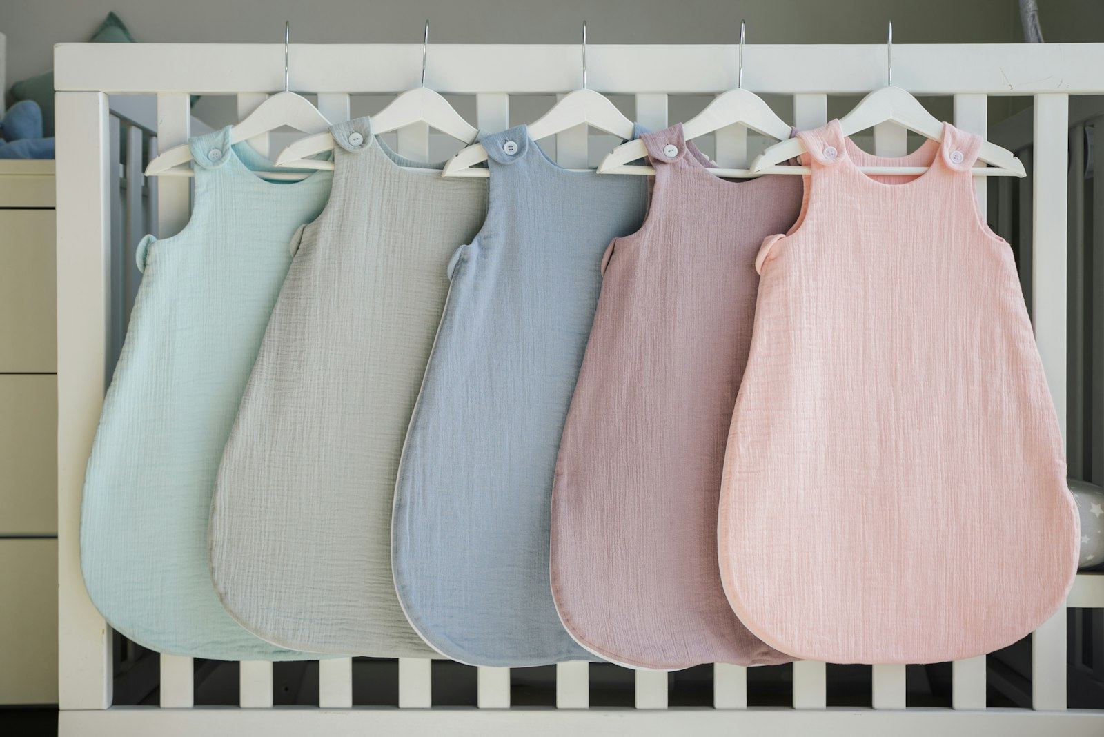Five pastel sleep sacks hanging on a crib rail