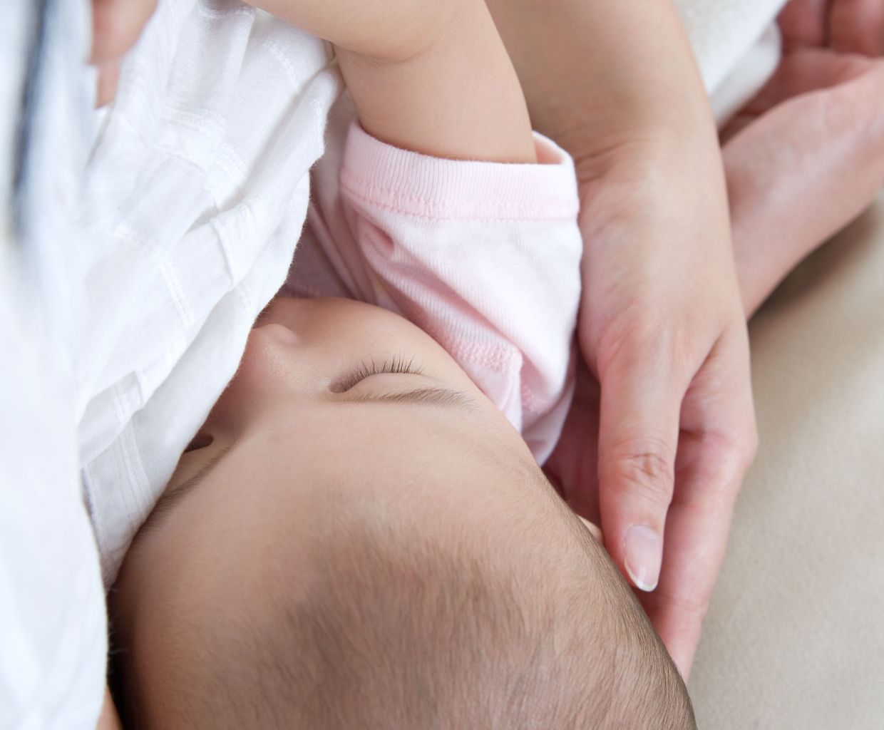 Close-up of a baby breastfeeding while the mother's hand supports the baby's head