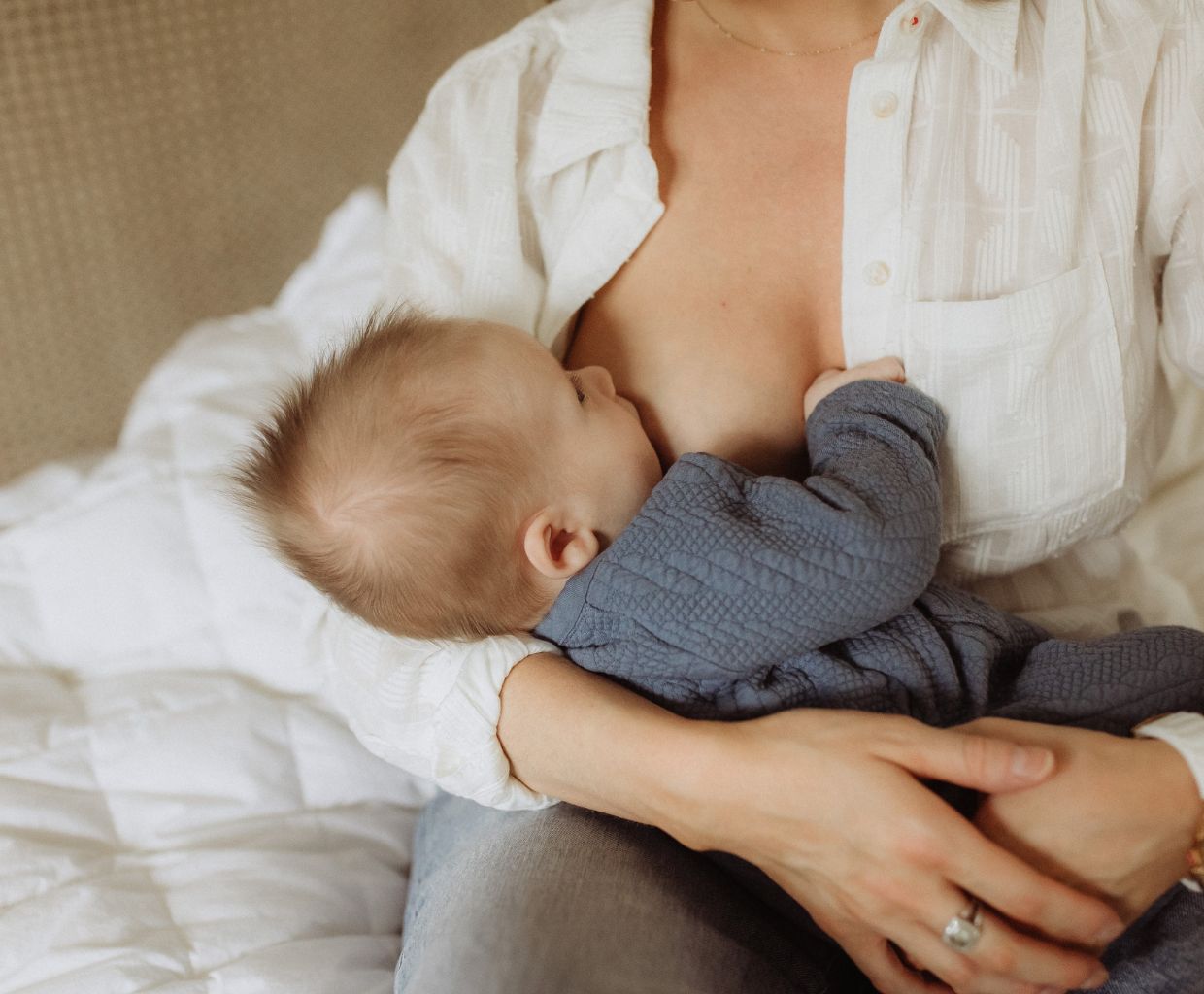 Baby in a blue knit top breastfeeding, cradled in the arms of a mother in a white shirt