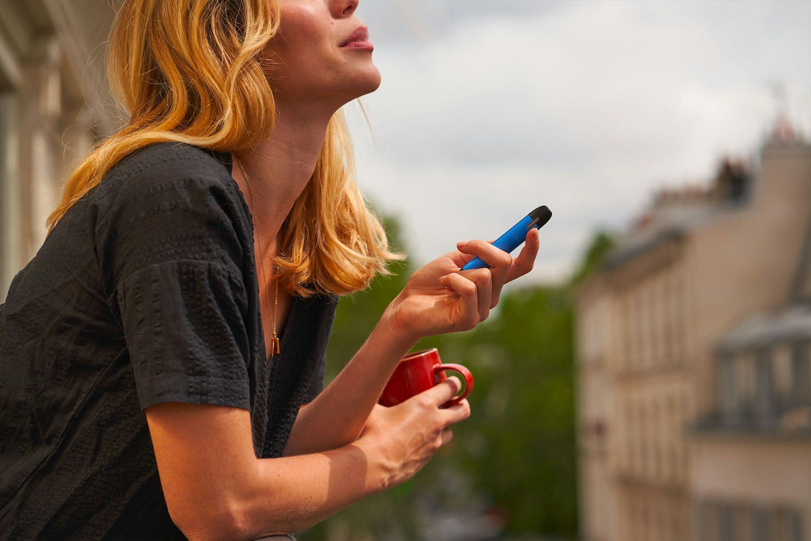 Woman on a balcony holding an e-cigarette and a cup
