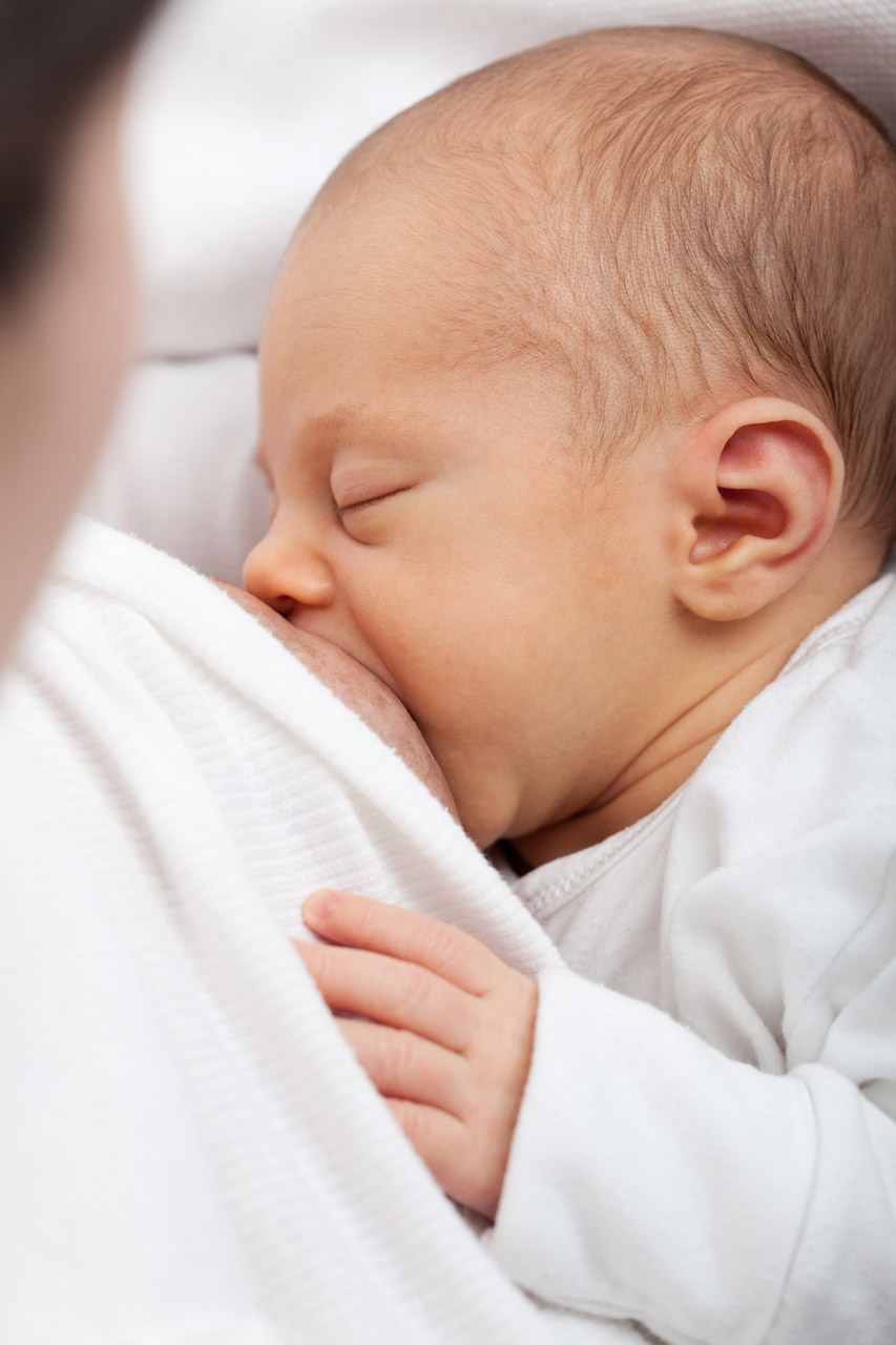 Close-up of a sleeping newborn breastfeeding, wrapped in a soft white blanket